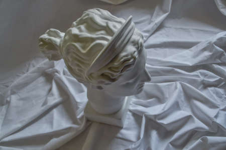 Ancient greek sculpture white plaster marble head of diana on a background of white fabric drapery with foldsの写真素材