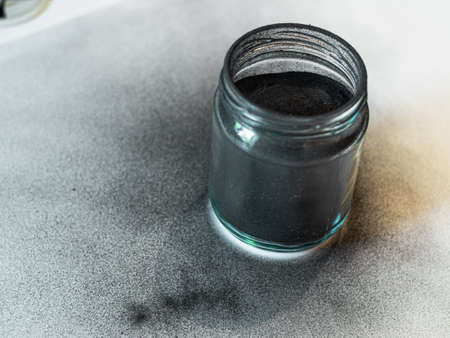 Activated carbon powder for cosmetic face mask in a jar, side view, blue shadow and white background