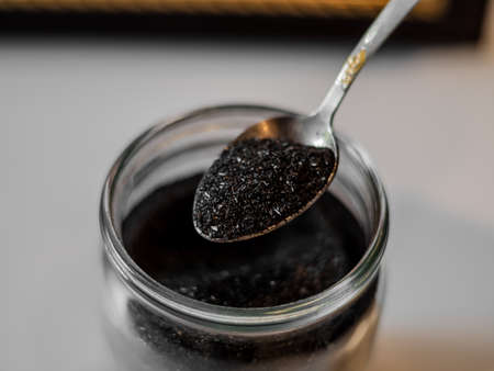 Homemade face mask and scrub with activated powder in glass jar on gray back, iron spoon with coal