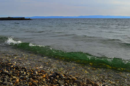 bright emerald green waves of lake baikal in the light of the sun in summer, blue mountains on the...