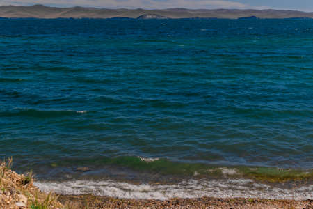 bright blue emerald waves of lake baikal in the light of the sun in summer, mountains on the...