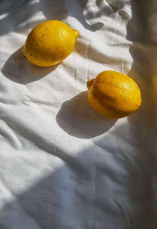 two yellow lemons on a white cloth with folds in sunlight with shadowsの写真素材
