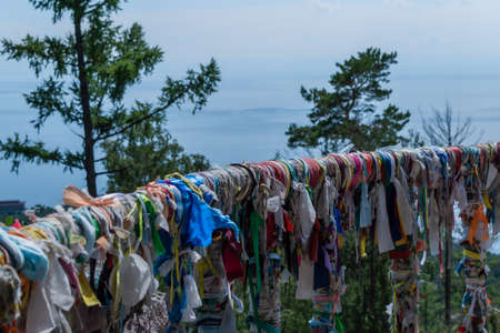 multicolored ribbons on the railing of the terrace against the backdrop of the landscape of blue lake Baikal, coniferous treesの写真素材