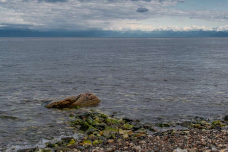 stone green path on a pebble coast in a blue lake baikal against a background of mountains and sky with cloudsの写真素材