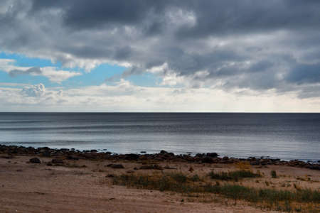 sandy shore with grass on coast of blue Ladoga northern lake at sunset with clouds in the skyの写真素材