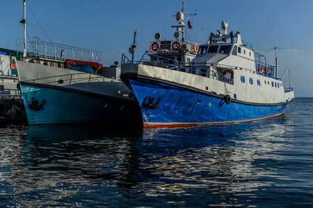 white blue ships boats on pier in bay of lake baikal with reflections in water in light of sunsetの写真素材