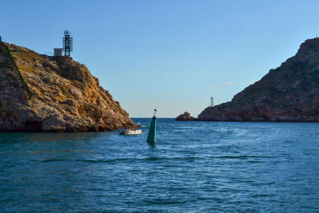 strait between two rocks, mountains with ships, boats and buoys against blue sky, balaclava town, Crimea in Black sea, sunsetの写真素材