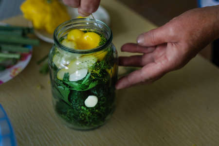 the process of salting cucumbers and squash in a jar on the table. Marinating crops in the kitchen in the fall. Women's handsの写真素材