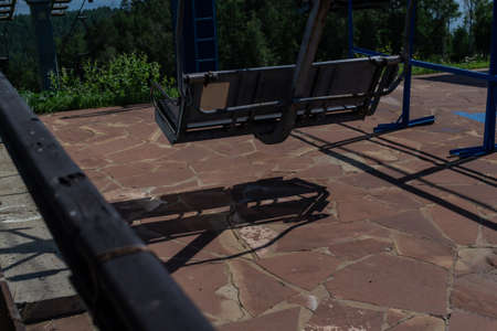 empty cable car seat stands in parking lot waiting for people in sunlight with shadow on the forest...