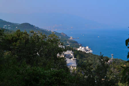 top view of resort town with white buildings on shore of Black Sea bay among mountains, blue water,...