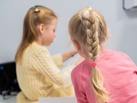 Little girls with blond hair are reading a note on a sheet. Back view. Girl in a pink sweater and...