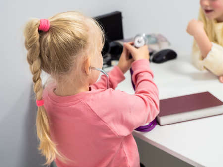 Back view portrait of little girls in pink sitting in doctor's office and playing medicineの写真素材