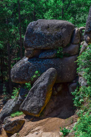 Large geometric stone rocks in light of sun lie on top of each other with shadows in forest between...