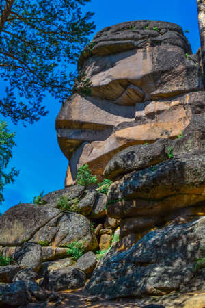 Large geometric stone rocks form of face profile in light of sun. Krasnoyarsk pillars, nature park in Siberia. Blue sky, summerの写真素材