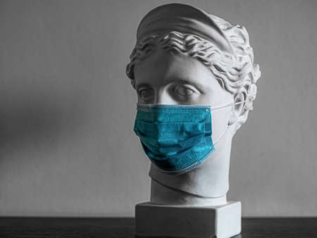 Plaster copy of the head of an ancient statue of Diana on a light textured back. Woman's face with plaster of paris sculpture in medical mask. Virus Covid-19. Pandemicの写真素材