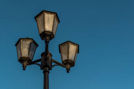 Old vintage black decorative lantern with clear glass on pillar. Three street lamps on one pole in...