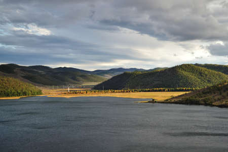 Autumn view of yellow grass shore of bay Lake Baikal with hills and mountains covered with green...