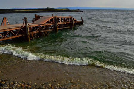 Old rusty iron pier, red orange bright dock construction on sandy stone shore of Lake Baikal in...