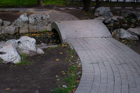 White stone trail and bridge over small pond among stones and rocks in city park. Autumn fallen...