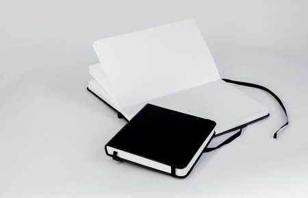 Black small closed notepad and large open notebook with blank white pages and ribbon bookmark lie...