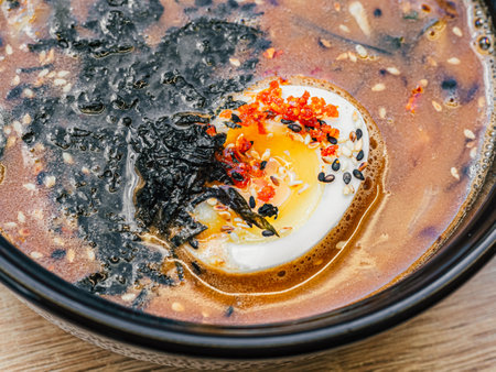 Cut egg, sesame seeds, nori in red golden broth of Hot miso soup in black and white plate on table. Top view. Dish of Japanese cuisine in Asian restaurant, cafe. Close upの写真素材