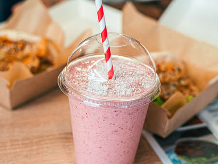 One pink fruit milk cocktail in plastic cup with white-red spiral pattern tube for milkshakes stand on table in street cafe. Fast food background, backdropの写真素材