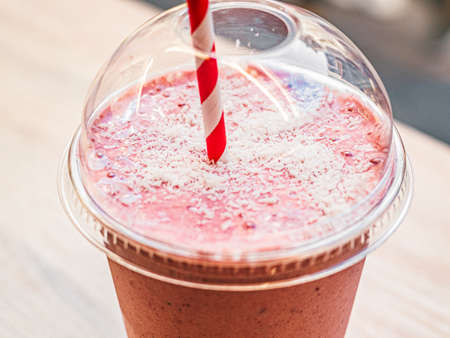One pink fruit milk cocktail in plastic cup with white-red spiral pattern tube for milkshakes stand...