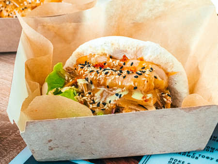 Bao with tofu in paper in paper carton box. Rice buns with vegetable, soya filling with sauce, sprinkled with sesame seeds. Fast food in a cafe, restaurant. Close-upの写真素材