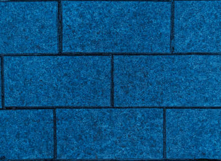 Brickwork of bright big blue geometric horizontal bricks bonded with cement grout between square...