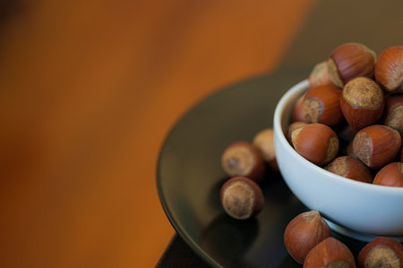 Heap, pile of brown nuts, hazelnuts lies in a small white plate and a black plate on table on blurry warm background. Close-up. Place for textの写真素材