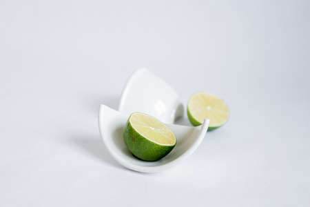 Cut halves of lime in a broken half of a ceramic small platter on a white background. Place for text.の写真素材