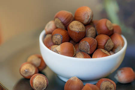 Heap, pile of brown nuts, hazelnuts lies in a small white plate and a black plate on table on blurry...