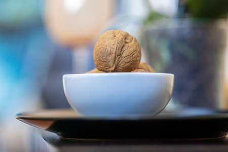 Heap, pile of whole walnuts in a round-shaped brown shell lie in a small white platter on black plate on a blue green blurred bokeh backgroundの写真素材