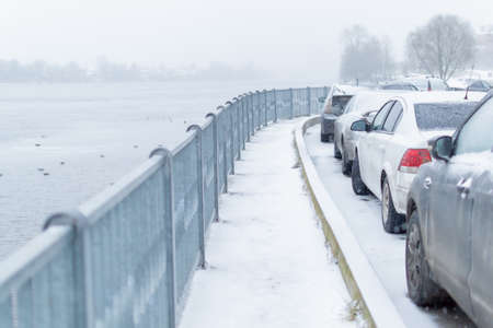 Small rounded snowy embankment next to the road, there are cars, behind the river with ducks, fog, trees in the park. Winterの写真素材
