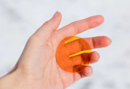 Small colored round transparent glass of golden yellow color in the hand of a man against a backdrop...