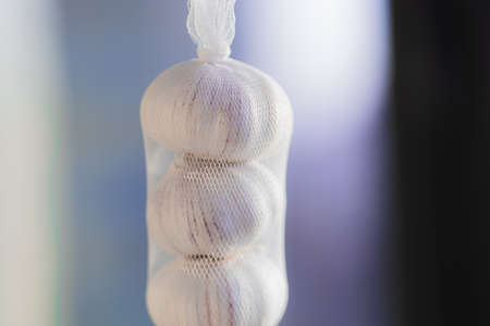 three white garlics stand on top of each other in a grid in sunlight against light violet blurred bokeh backgroundの写真素材