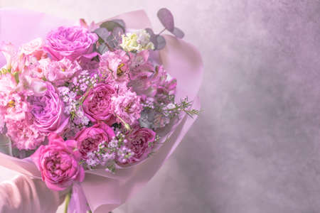 A lush bouquet of light pink, purple, white cute delicate small roses of different sizes, flowers of green leaves. Paper packaging. Place for textの写真素材