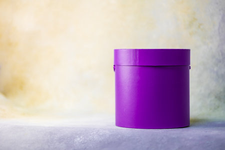 Round bright purple cylindrical flower box in the studio. Warm yellow background. Place for text