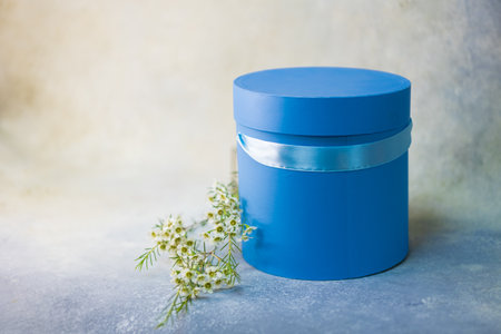 Round bright violet blue flower box cylindrical form with ribbon in the studio. Warm yellow...