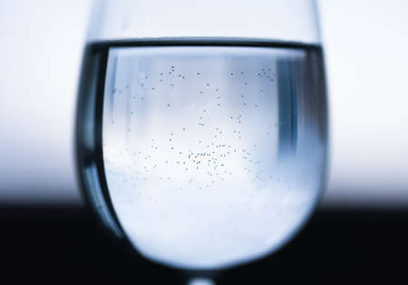 Transparent wine glass with water with reflection, small bubbles. Blue black white blurred background. Close-upの写真素材