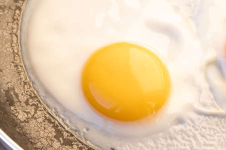Cooked small fried eggs with finish white and bright round raw yolk in a dark skillet, Edge cracks....