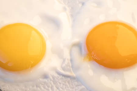Two bright round raw yolk in finish white, cooked small fried eggs is a simple breakfast. Top view,...