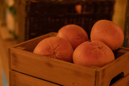 Several whole unpeeled grapefruits, citrus fruits lie in a wooden box in the warm light of a store products for making cocktails and juices, drinksの写真素材