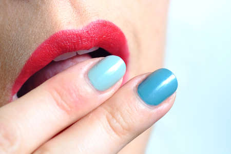 Close up of pastel and green fingernails touching beautiful and sensual red lips