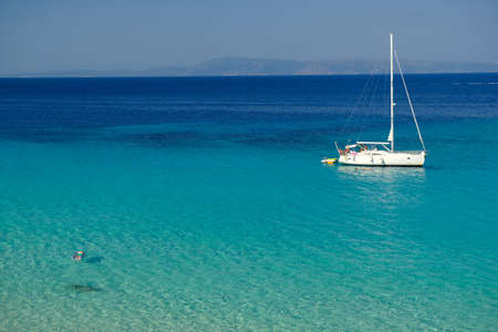Chalkidiki, Greece - August 14, 2017 : A sailboat and a single person swimming in the crystal clear waters of chalkidiki Greeceのeditorial素材