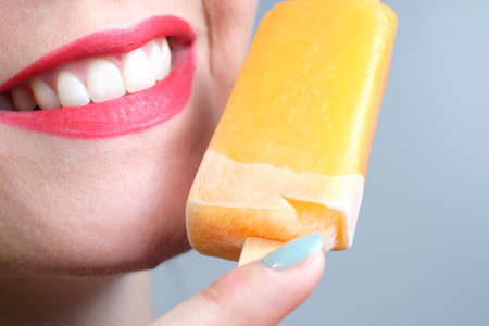 Closeup of a young woman eating ice cream with a yellow stick