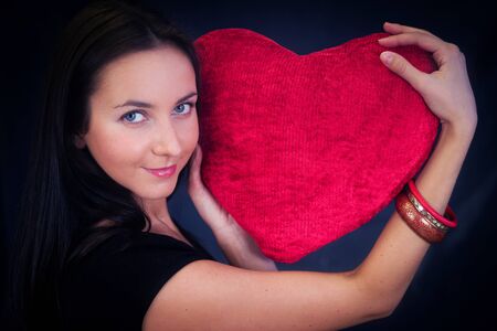 Woman with red heart shaped cushion on dark background