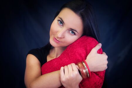 Woman with red heart shaped cushion on dark backgroundの写真素材