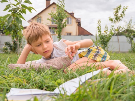 Reading the book concept. Publishing background. Smart child reading the book outdoor on the grass.の写真素材