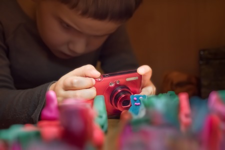 Boy focused on taking a picture. Child 4 - 5 years taking picture of crafted toys. Toys crafted by hand. Young photographer. Role games. Handmade toys background. Child taking photo. Close-upの写真素材